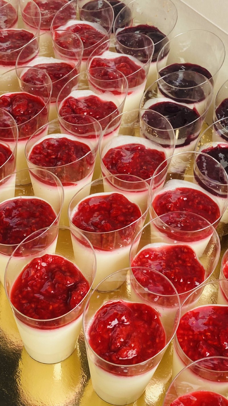 Kilka deserów panna cotta z warstwą malinowego musu w przezroczystych kieliszkach