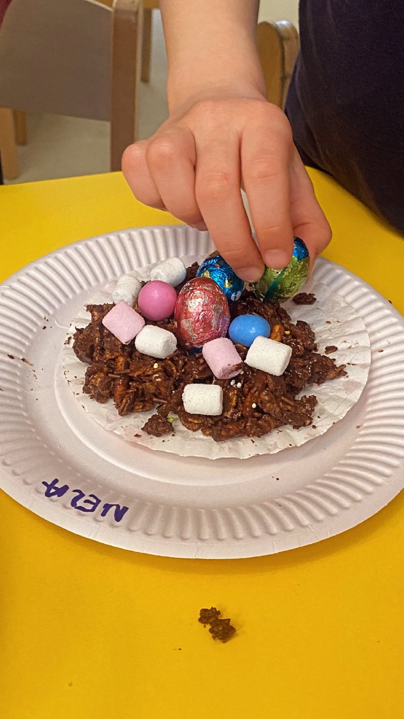 Dziecko dekoruje czekoladowego deseru piankami i cukierkami na papierowym talerzyku.