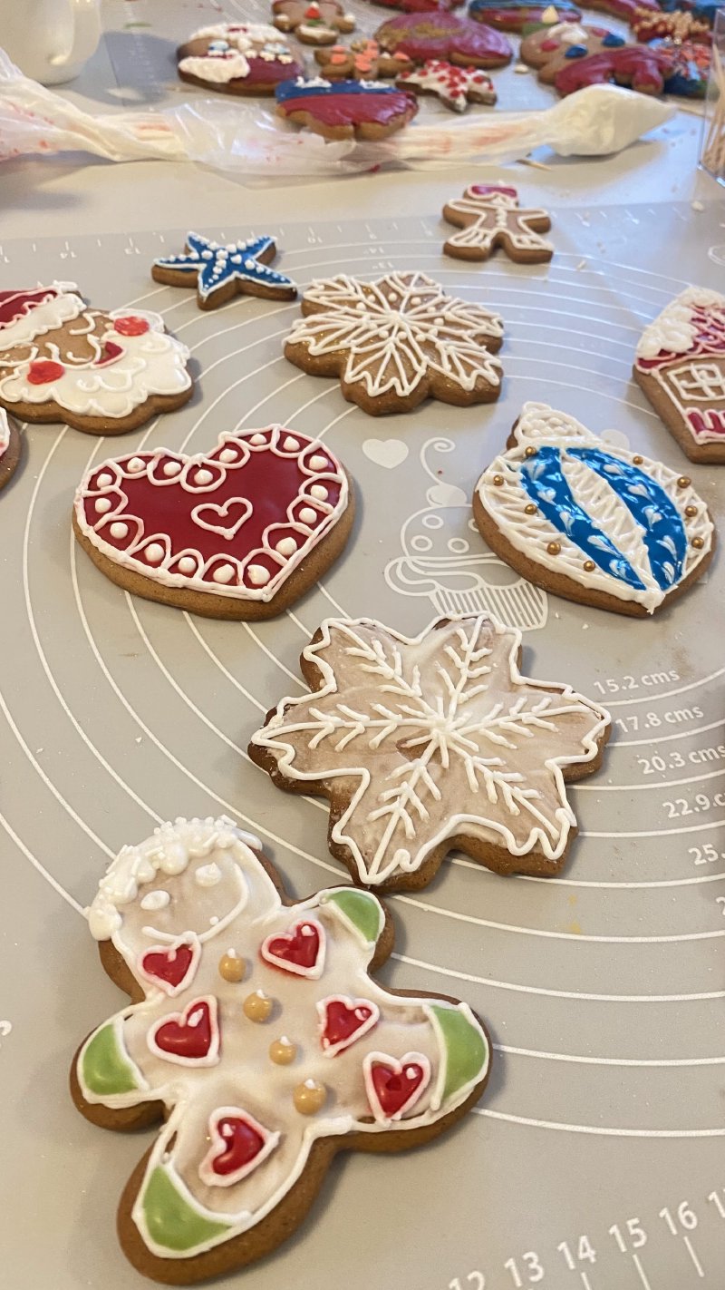 Kolekcja ręcznie lukrowanych pierników w kształtach serc, gwiazd i ludzików na szarej macie cukierniczej.