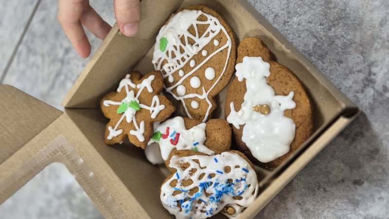 Zestaw lukrowanych pierniczków w pudełku otwierany przez dłonie.