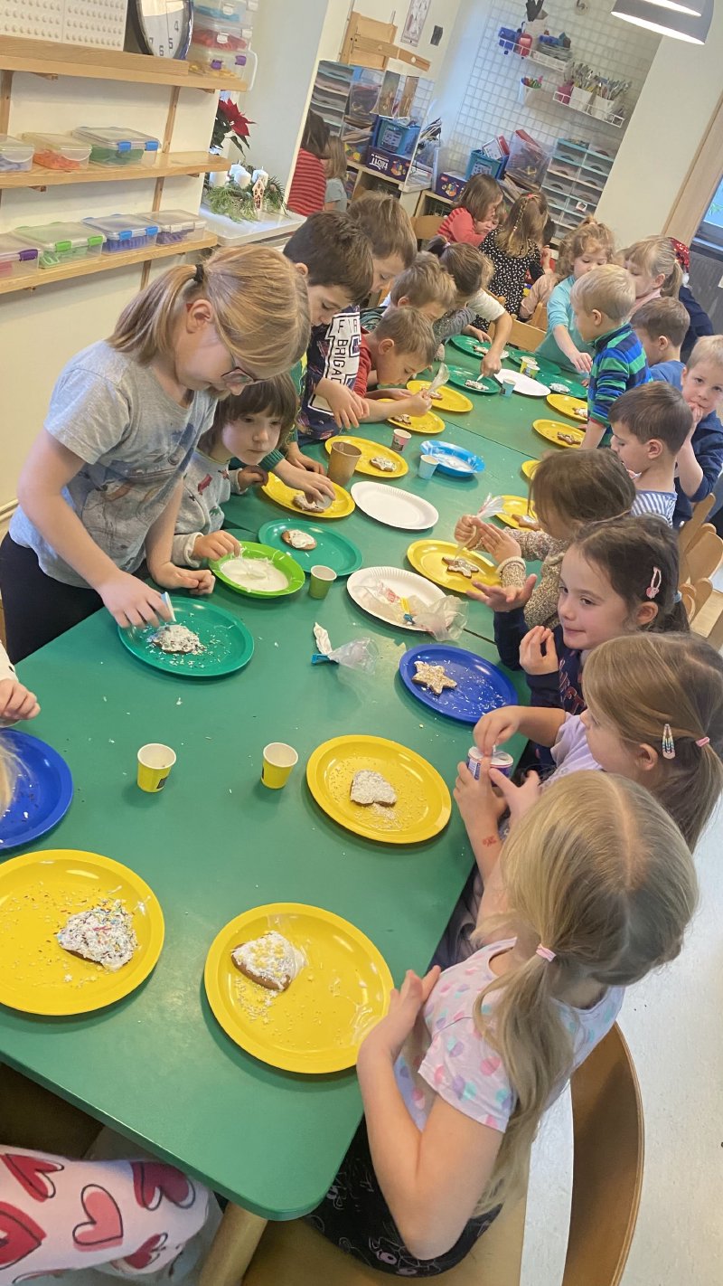 Dzieci w trakcie warsztatów cukierniczych dekorują ciasteczka na zielonym stole.