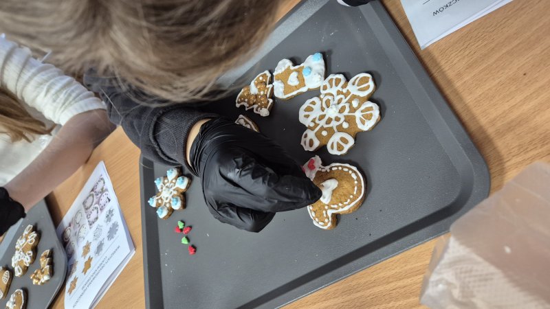 Osoba w czarnej rękawiczce dekoruje piernik lukrem podczas warsztatów.