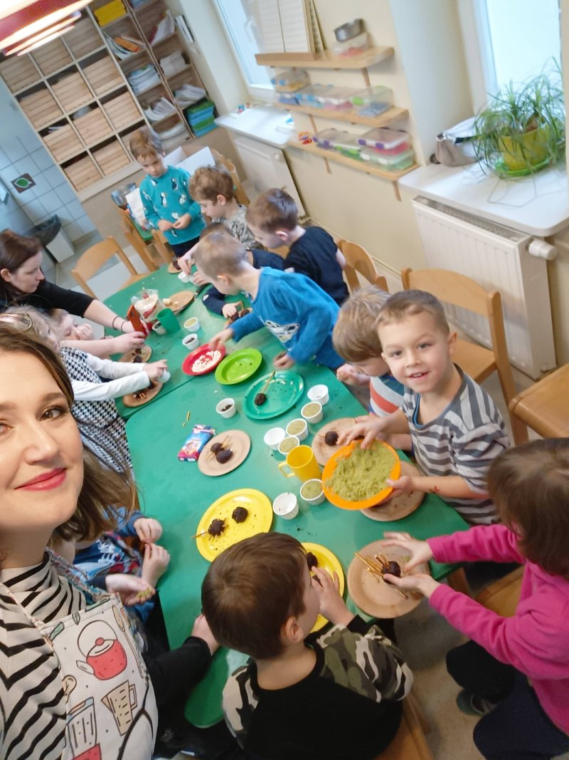 Grupa dzieci dekorująca czekoladowe kulki podczas warsztatów cukierniczych.